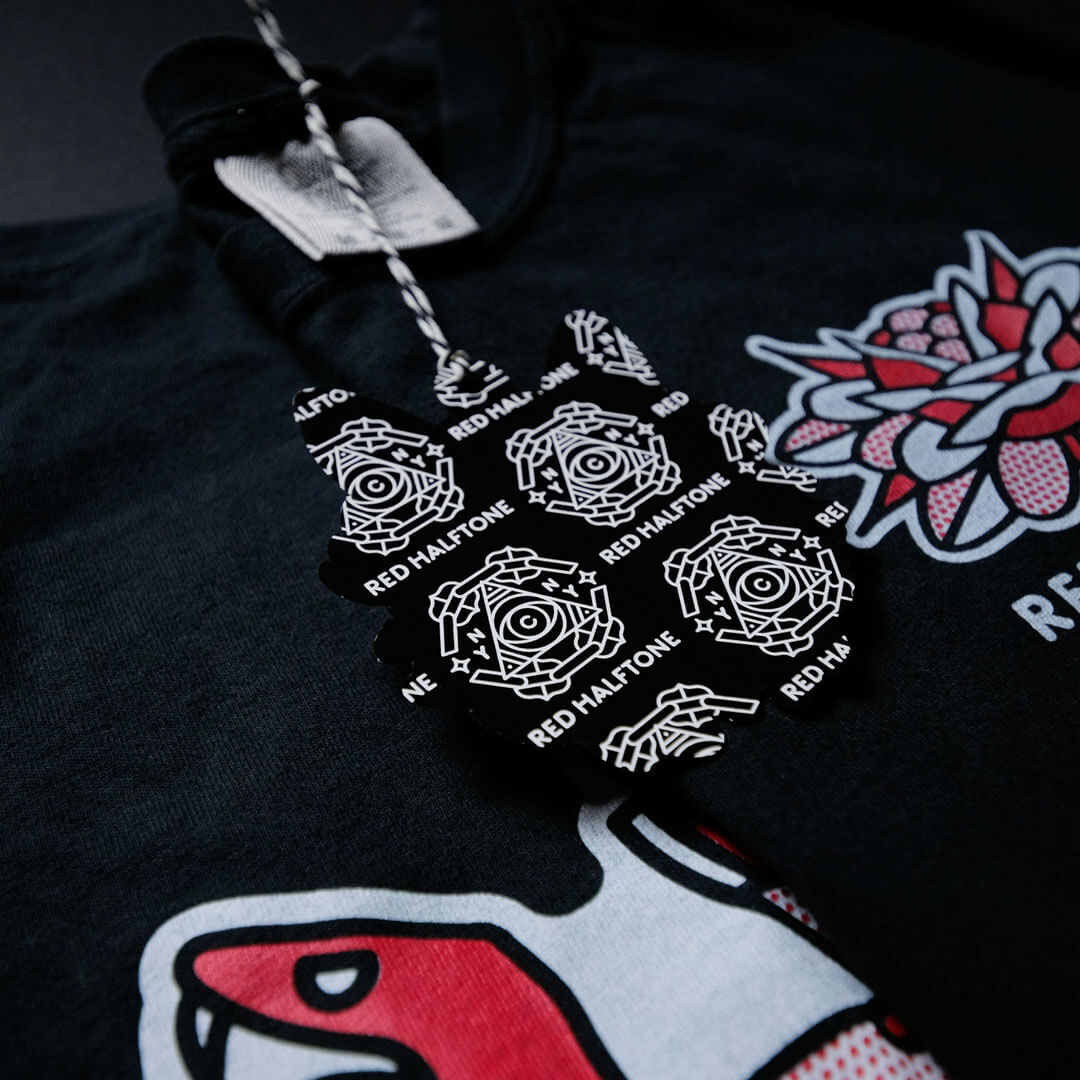 Black shirt with a red and white graphic design, featuring a floral motif. A black tag with geometric patterns and "RED HALFTONE" text is attached.