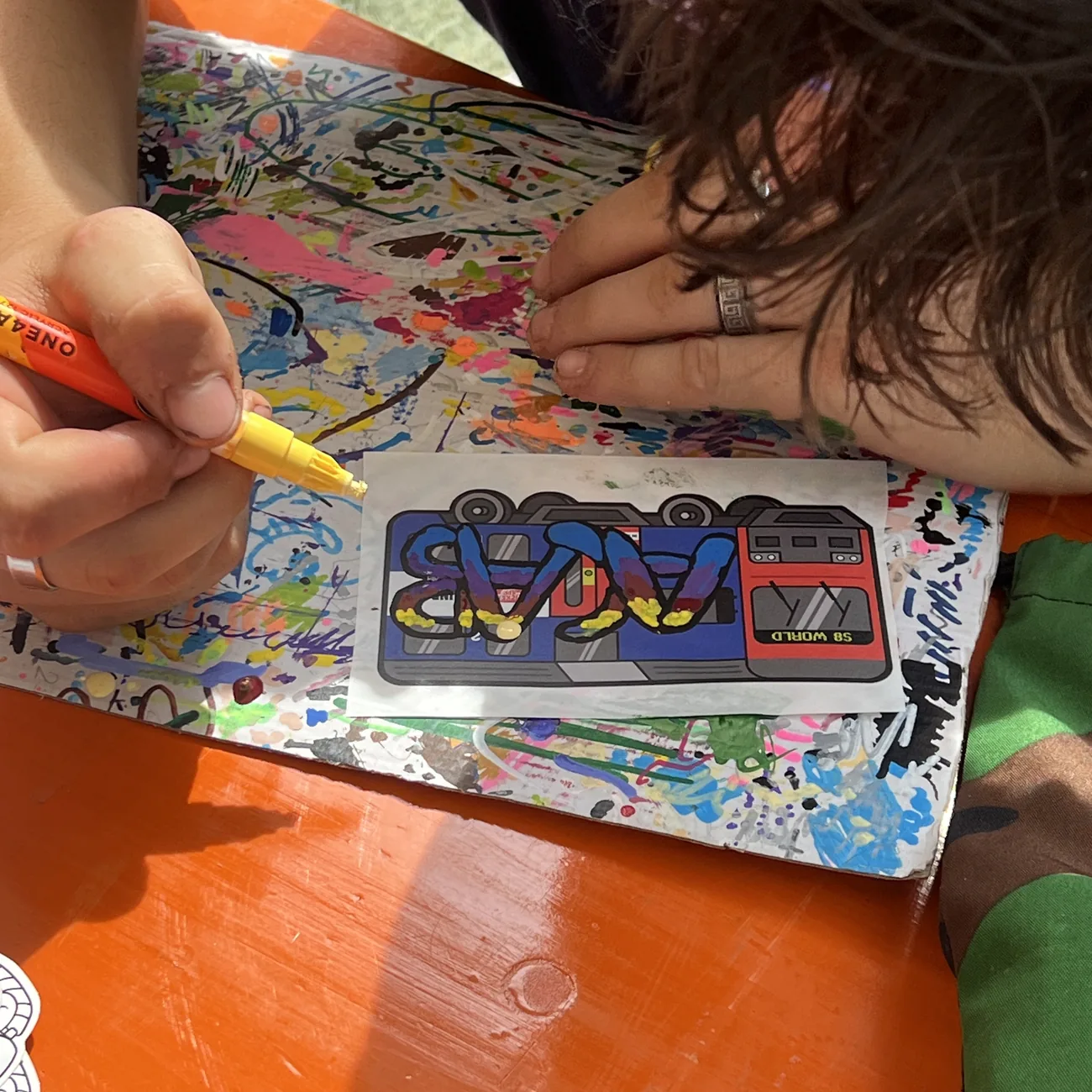 Hand colouring an S8 World train label with a yellow paint marker at the Brainfart x StickerApp workshop