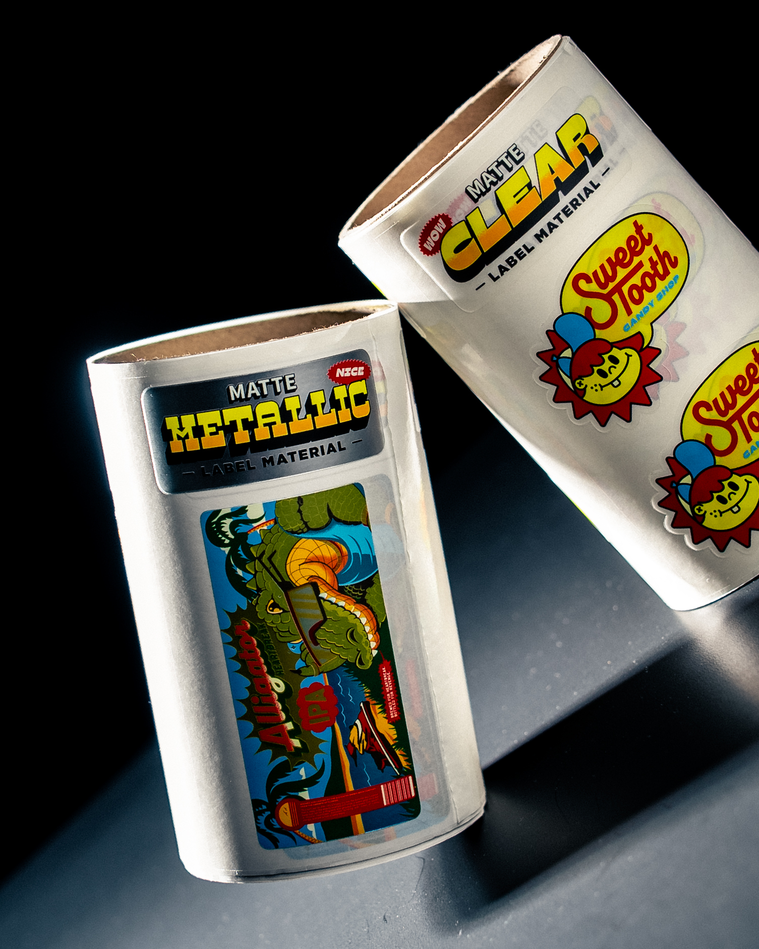 Two rolls of sample labels marked "Matte Metallic" and "Matte Clear", with an Alligator IPA label and Sweet Tooth Candy Shop labels