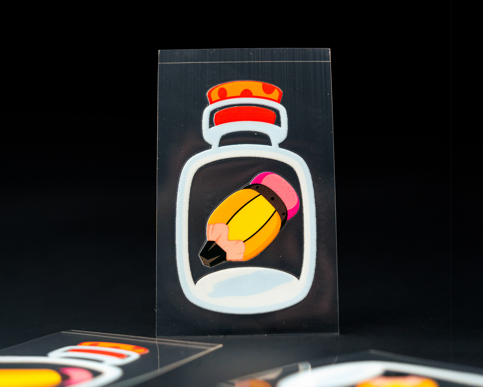 UV-dtf-sticker of a broken pencil inside a bottle, displayed against a black background, with parts of similar stickers visible.