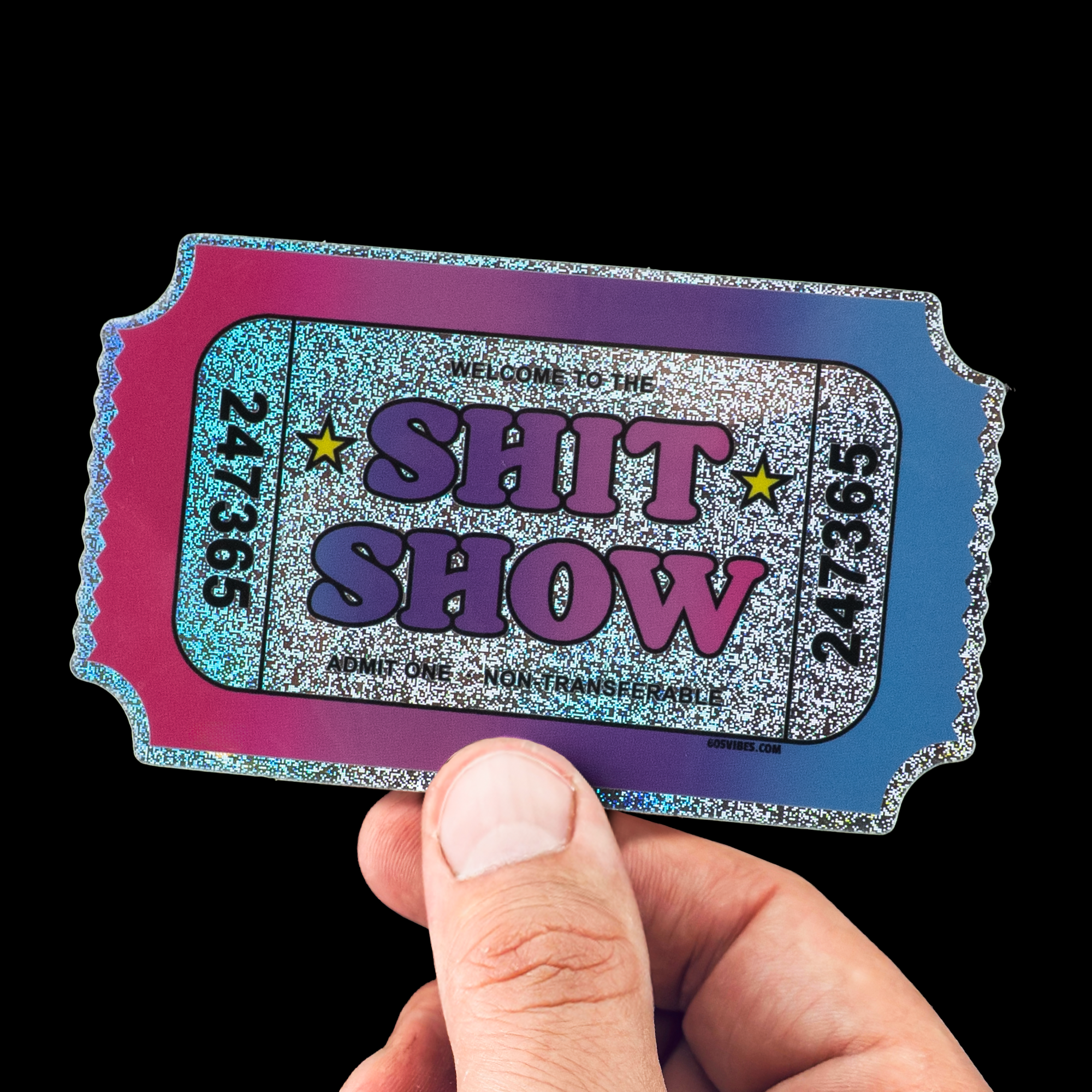 Hand holding a Pixie dust, multicolored sticker ticket with "SHIT SHOW" printed in bold letters, surrounded by stars and numbers.